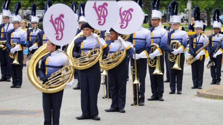 A jester stands on a bed for a marching band